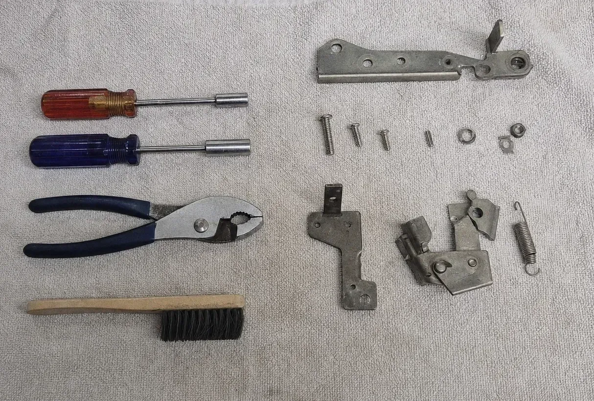 Red and blue nut drivers, slip-joint pliers, a hinge bracket and a tension spring laid out with screws and washers on a towel
